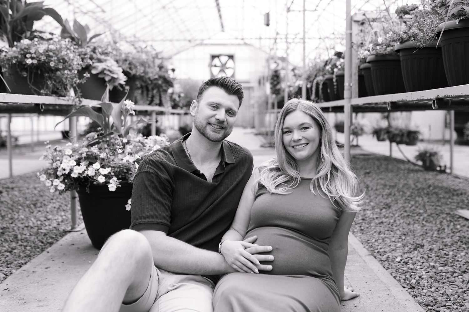 Black and white photo of couple sharing tender moment in greenhouse setting.