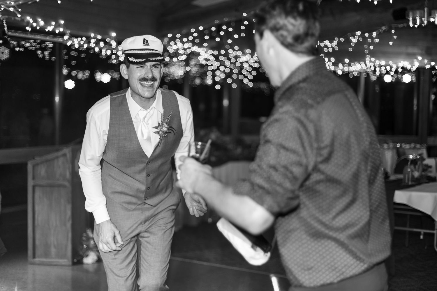 Black and white reception photos show couple's playful cake cutting moment under string lights.