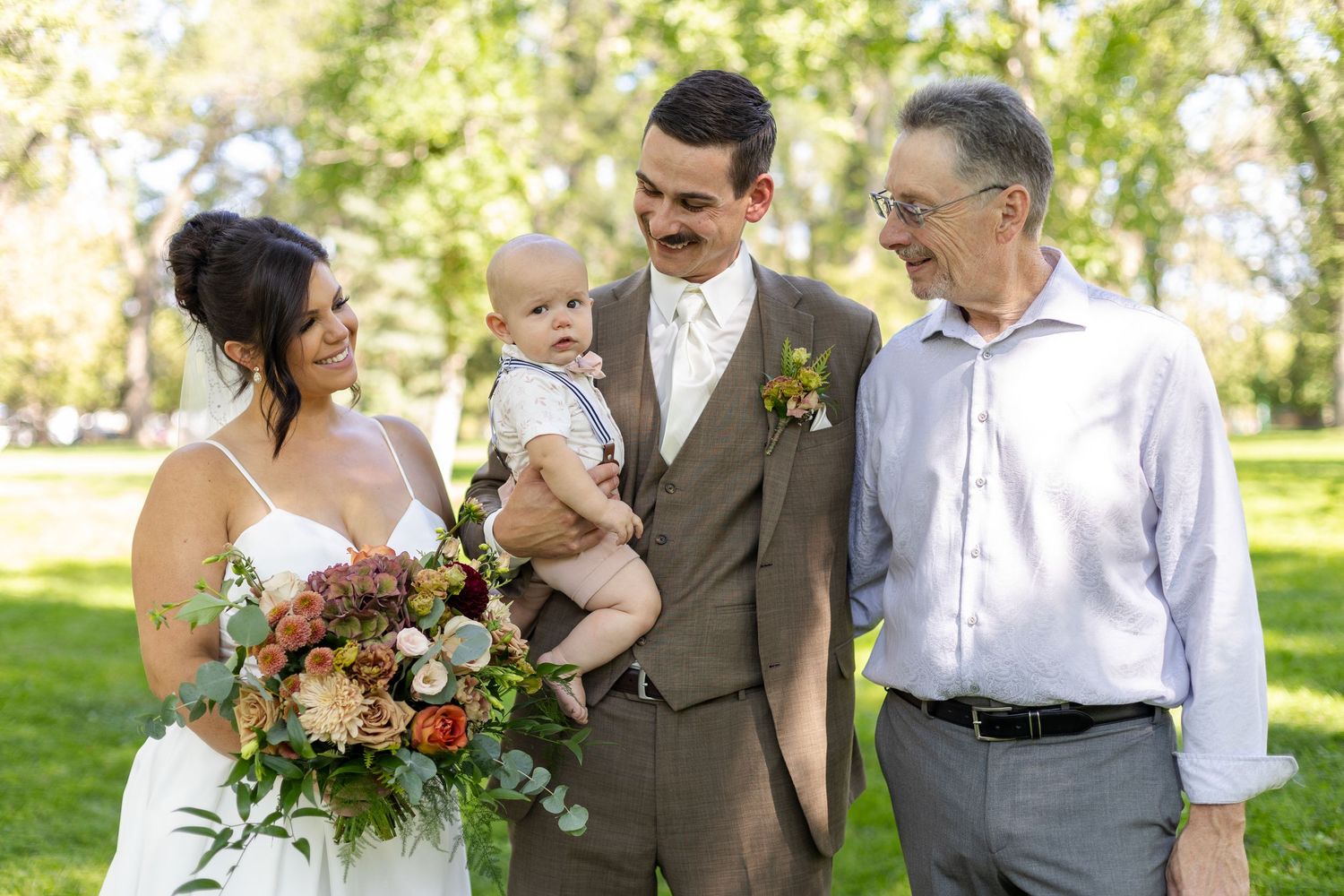 Wedding party gathered outdoors in formal attire with colorful bouquets and greenery.