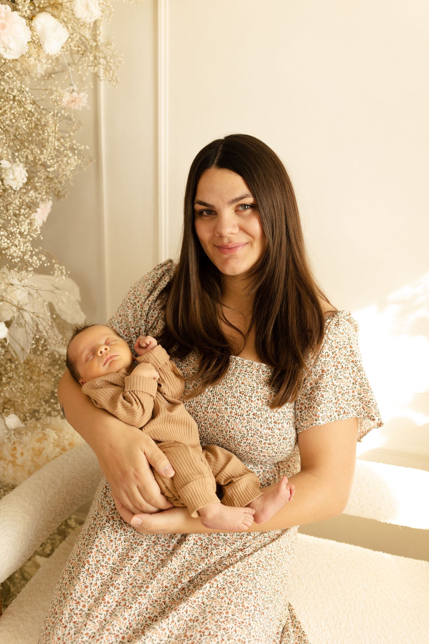 A tender moment between mother and newborn baby in a soft, naturally lit room with white decor.
