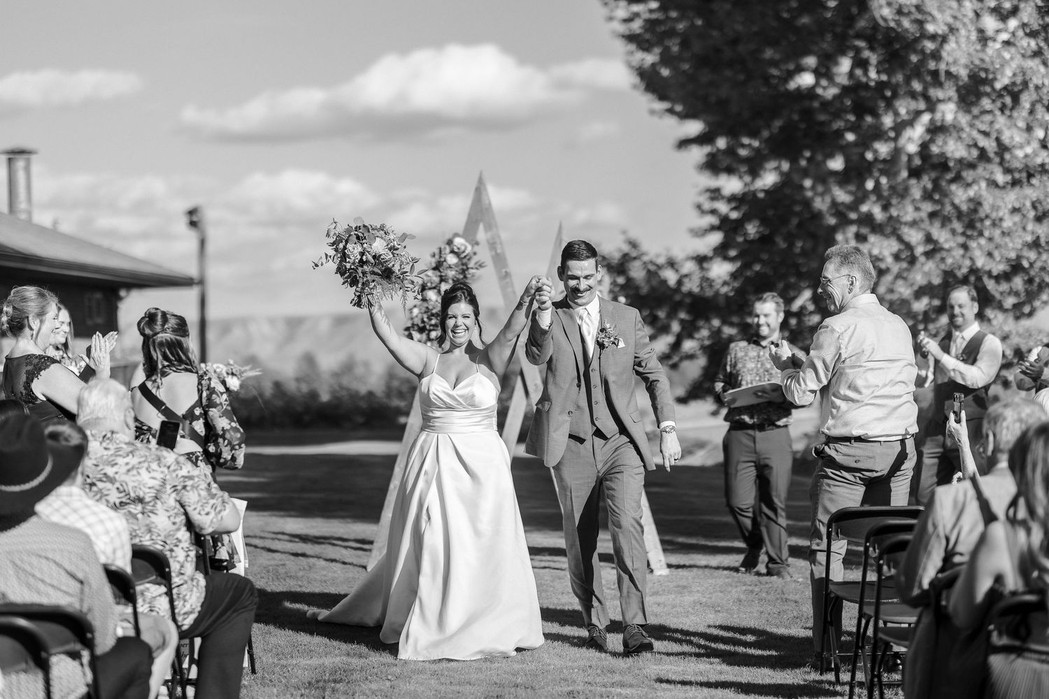 Wedding party and guests gather outdoors for celebration photos on a sunny day.