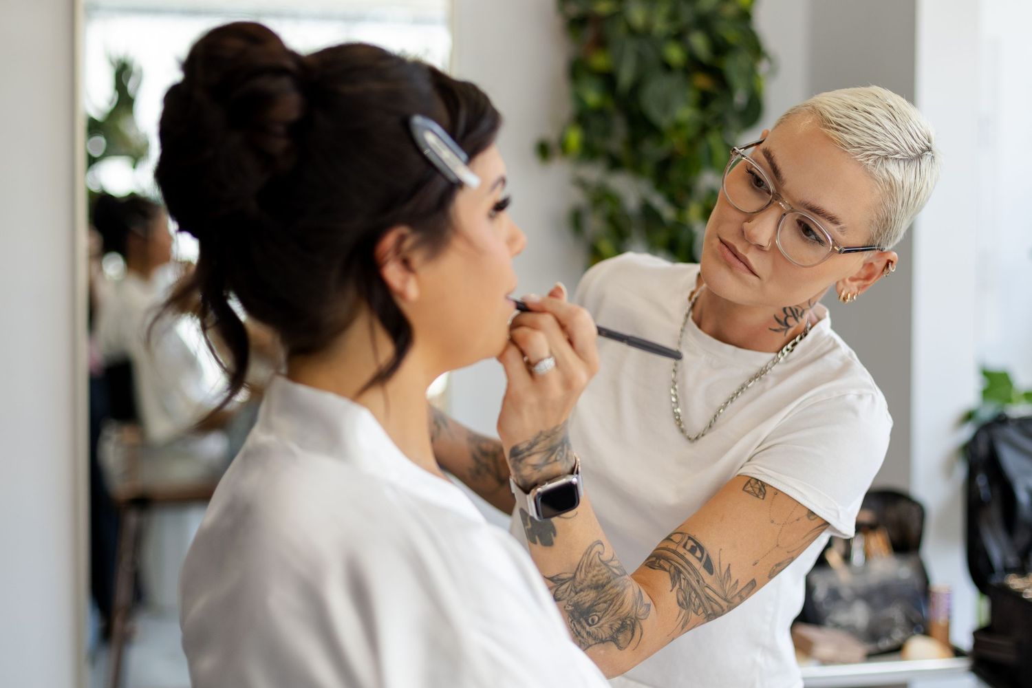 Professional makeup artist applying cosmetics to a client in a bright studio setting with indoor plants.