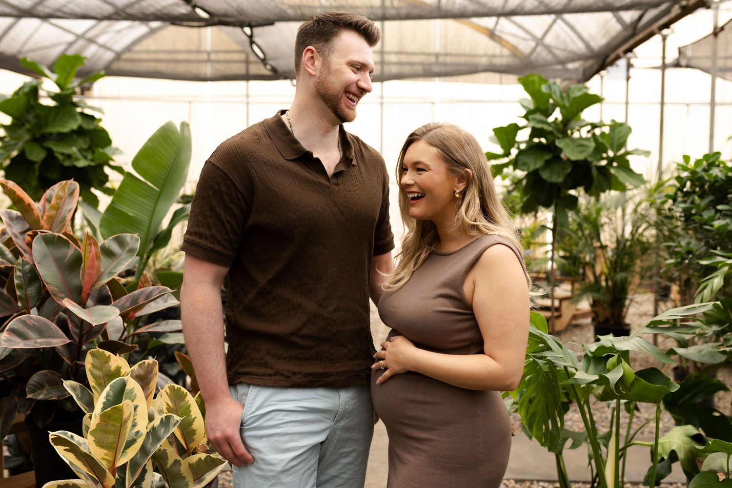 Happy couple sharing joyful moment in greenhouse filled with lush plants and natural light.