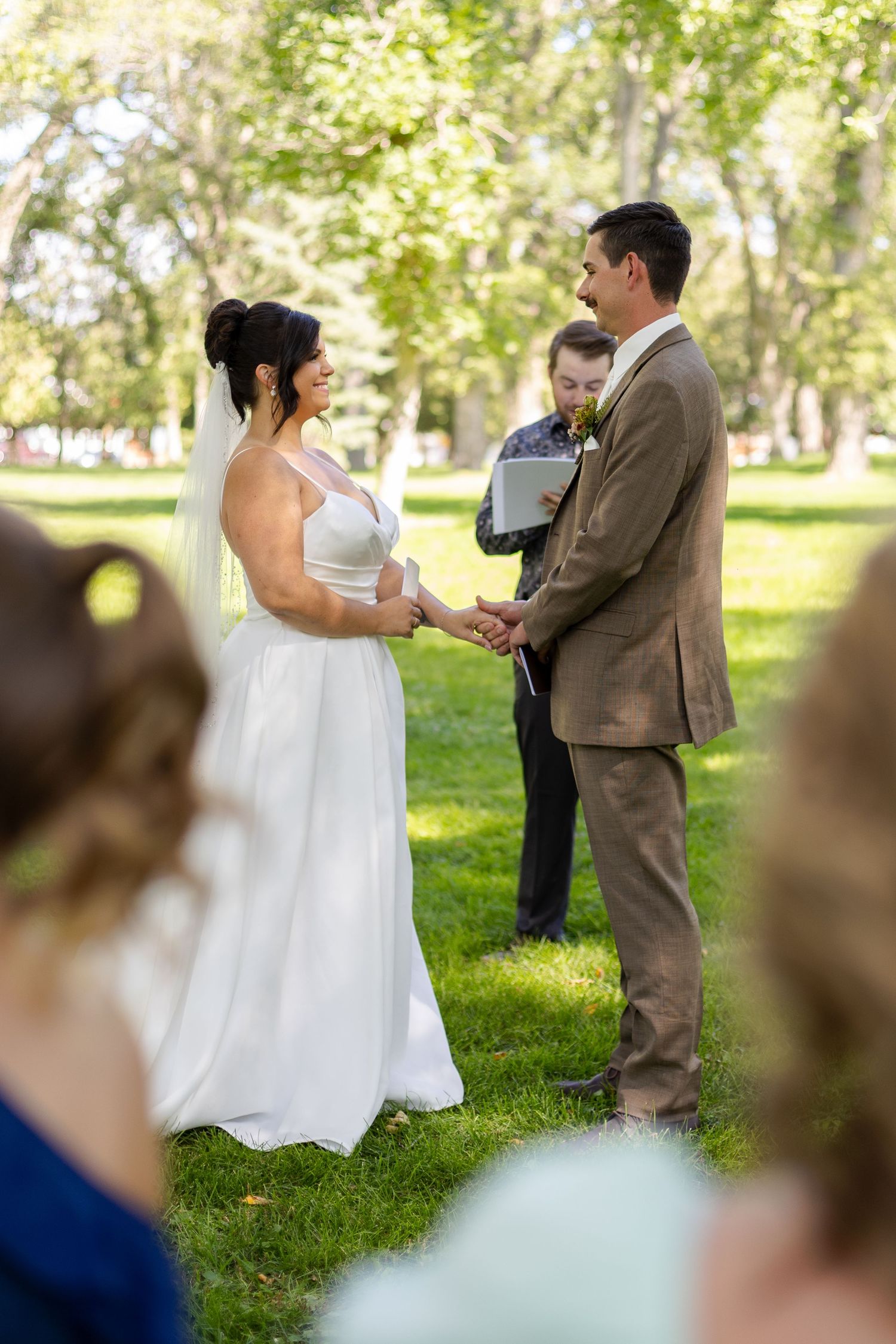 Wedding ceremony taking place in a sunlit park with guests watching.