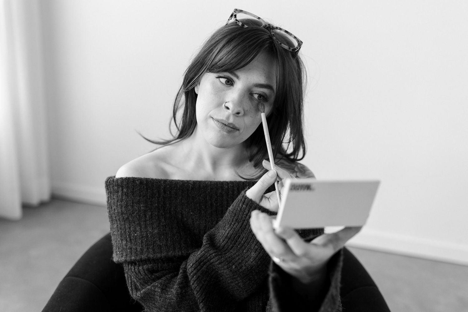 Person in black sweater lying on white couch with laptop and mobile phone in relaxed indoor setting.