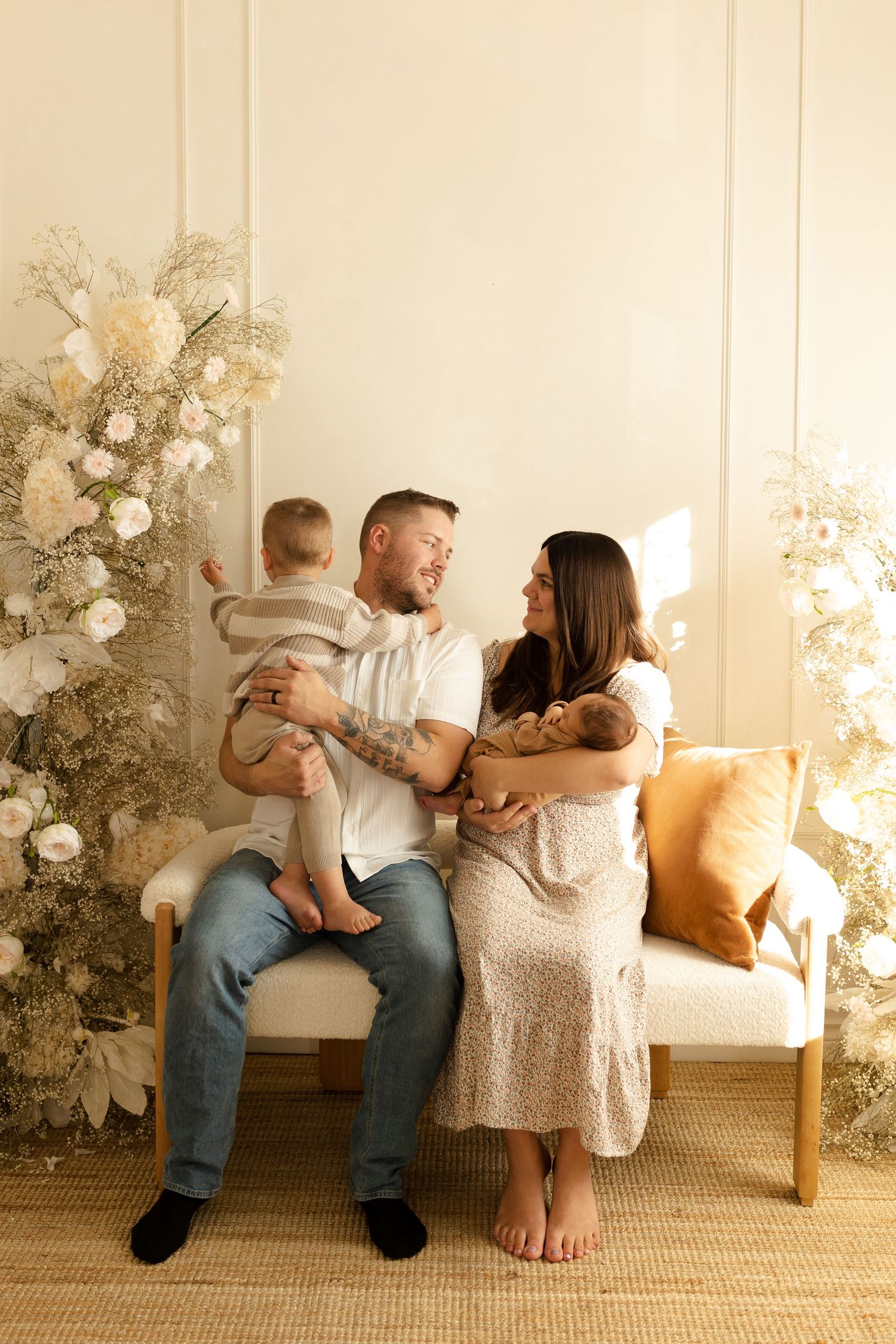 Family shares tender moments together while sitting on a couch with white floral decorations in the background.