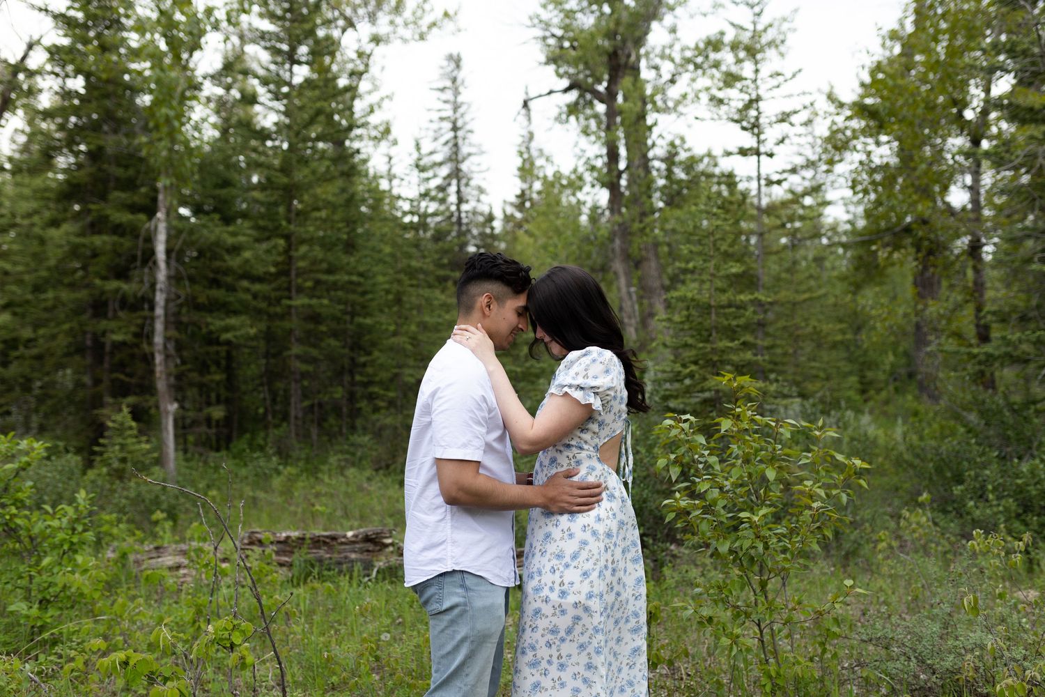 Romantic couple embracing in a natural forest setting with evergreen trees.