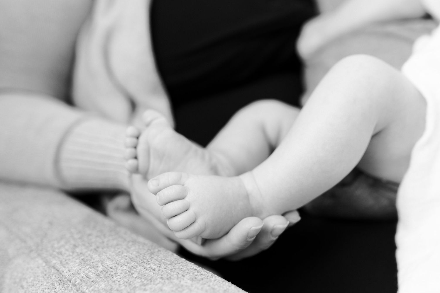 Close-up black and white photo of tiny newborn feet and hands.