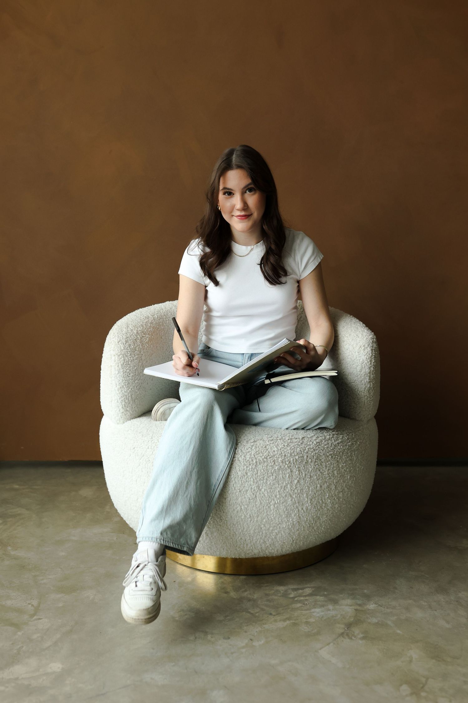 Lifestyle portrait of someone taking notes while sitting comfortably in plush cream-colored armchair.