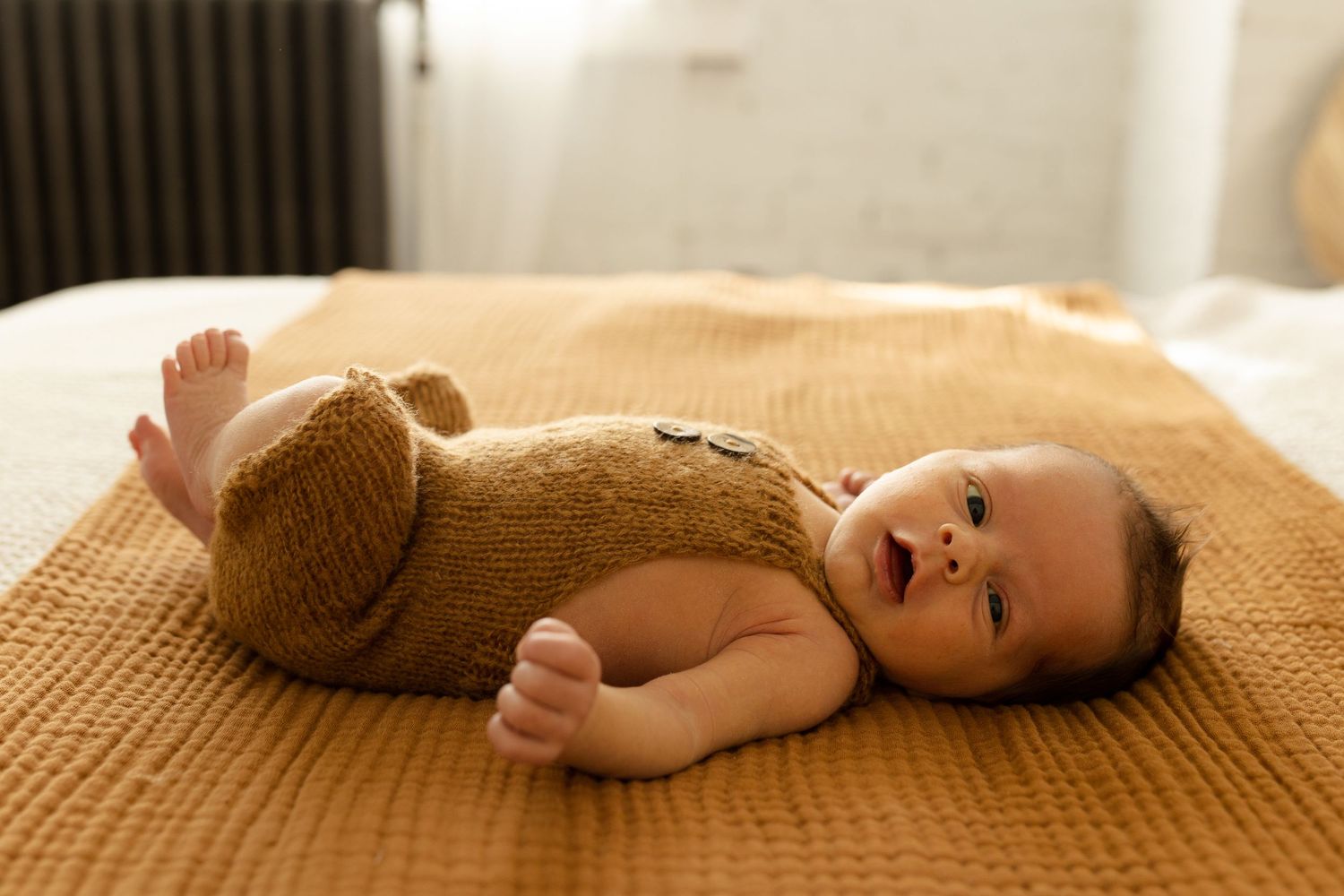 A series of connected photos showing a baby lying on a beige blanket wearing a brown knit outfit.