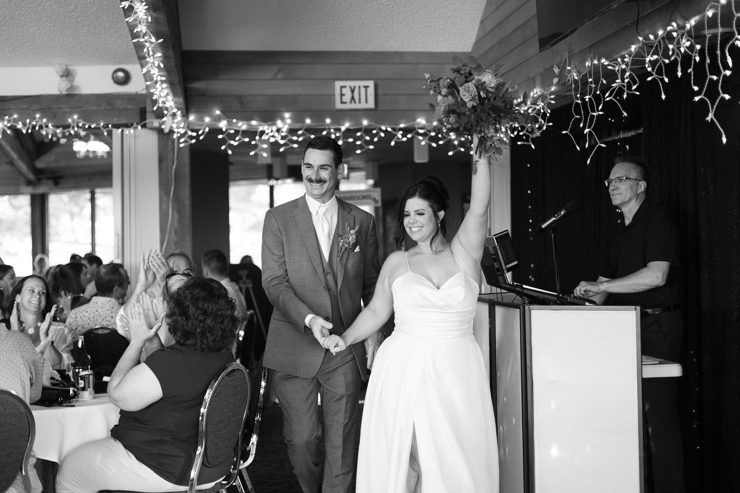 Wedding reception celebration with string lights and guests dancing in dimly lit venue.