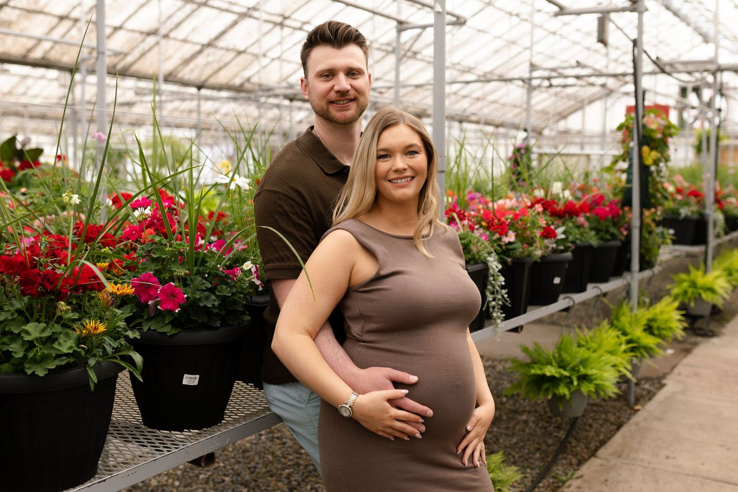 Greenhouse maternity photography with vibrant red flowers and greenery in background.