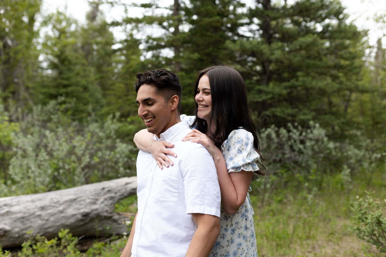 Romantic outdoor engagement photo session in a forest meadow with evergreen trees.