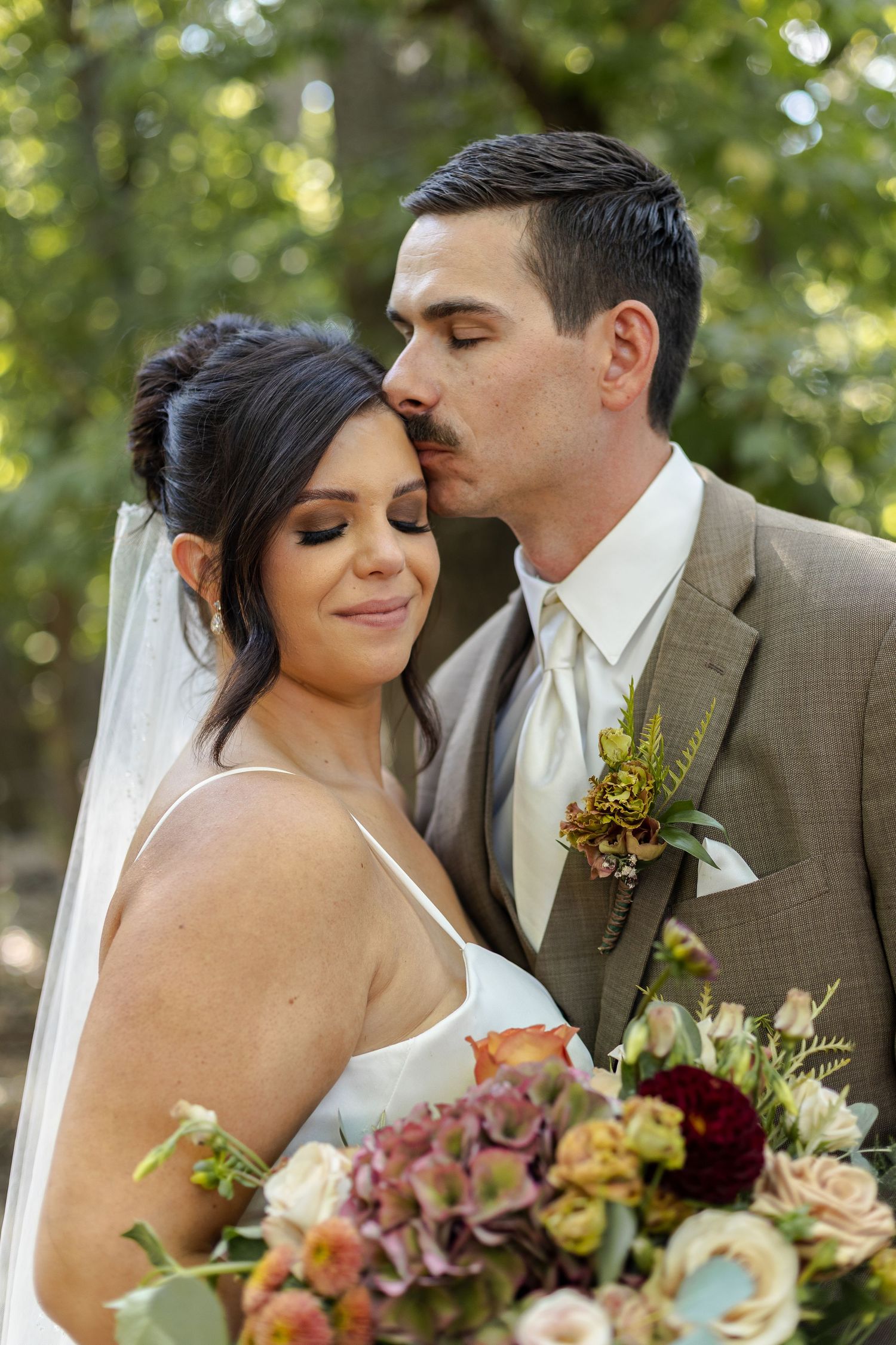 Romantic wedding couple embracing outdoors with autumn-colored floral bouquet.