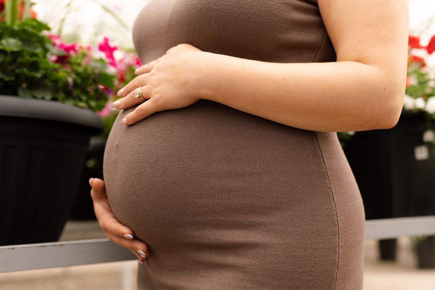 Close up of a pregnant belly in a brown dress with hands gently resting on top.