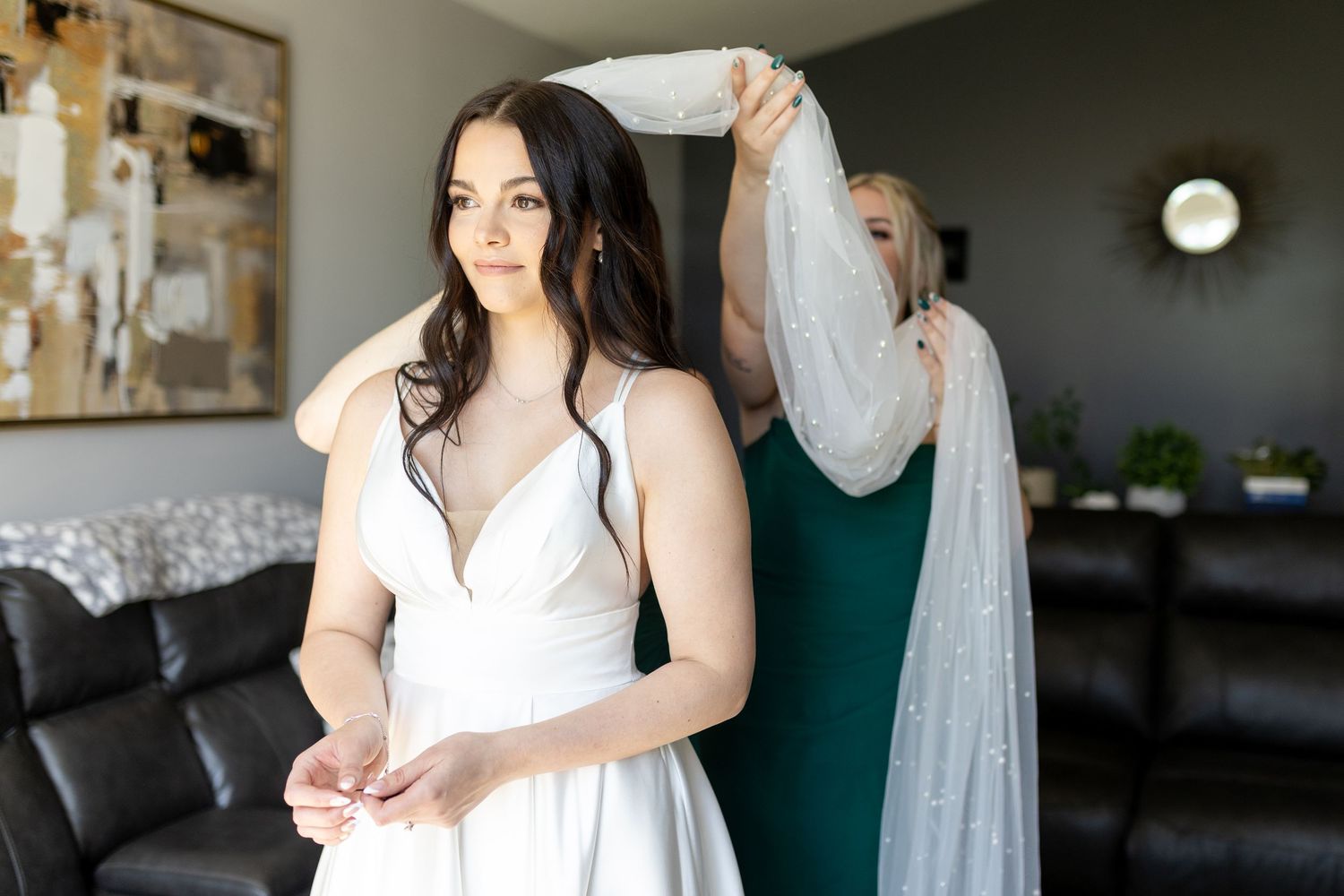 A bride in a white dress stands by a window during wedding preparations, creating an elegant bridal portrait.
