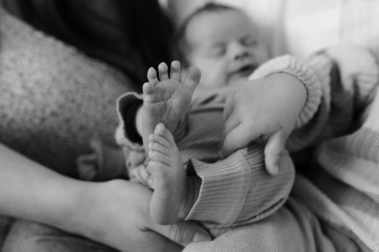 A sleeping newborn baby's tiny feet and toes are gently held in an adult's caring hands.