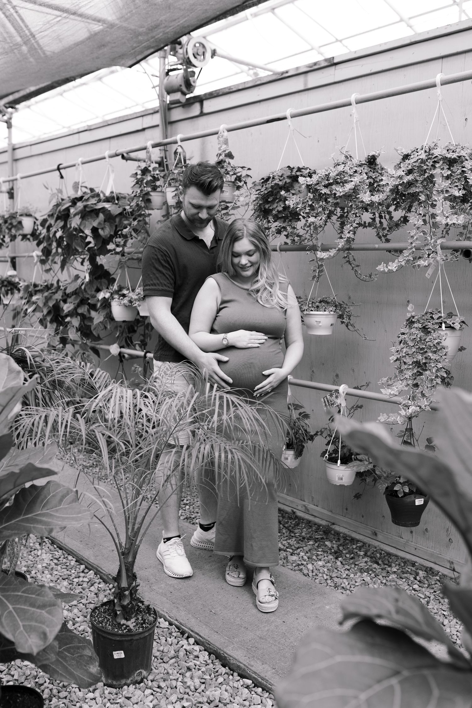 Black and white photo of a couple sharing a tender moment among greenhouse plants.