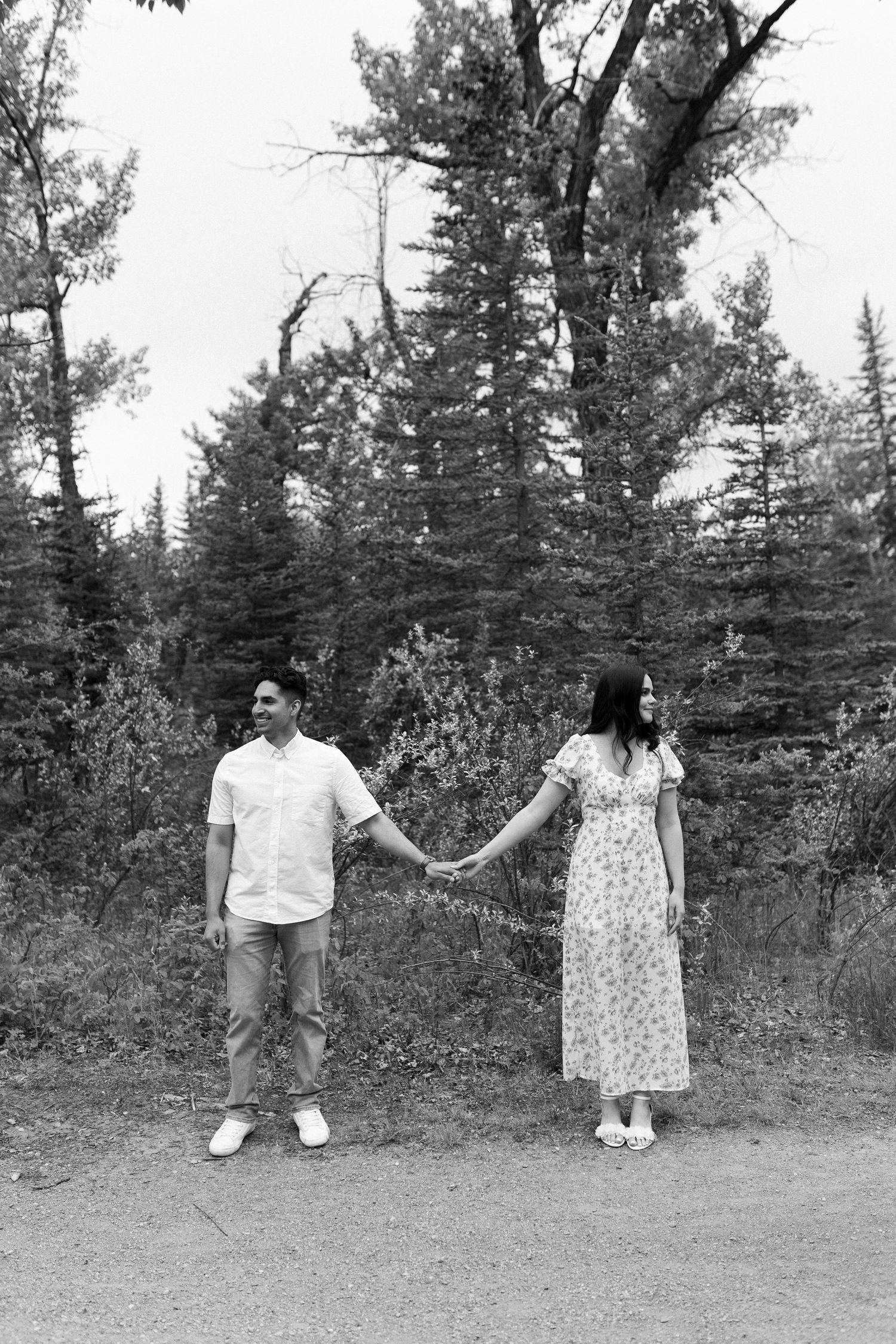 Black and white photo of two people playfully posing in a wooded area.