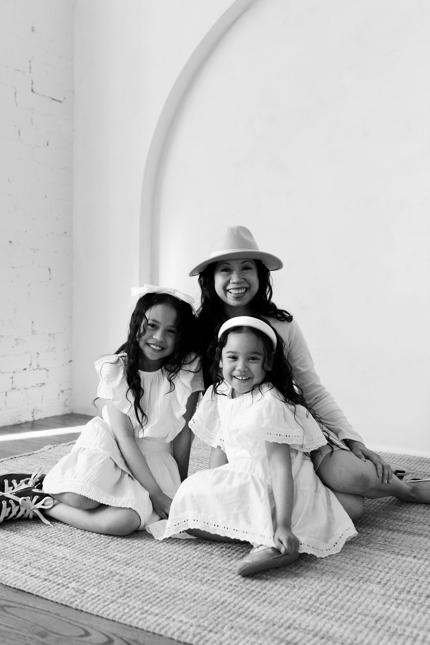 A black and white portrait of a family group sitting together on a rug wearing white dresses.