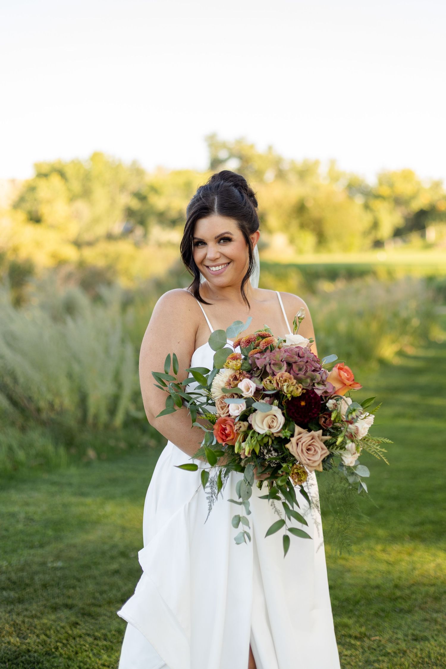 Beautiful autumn-toned wedding bouquet with roses and mixed flowers on golf course.