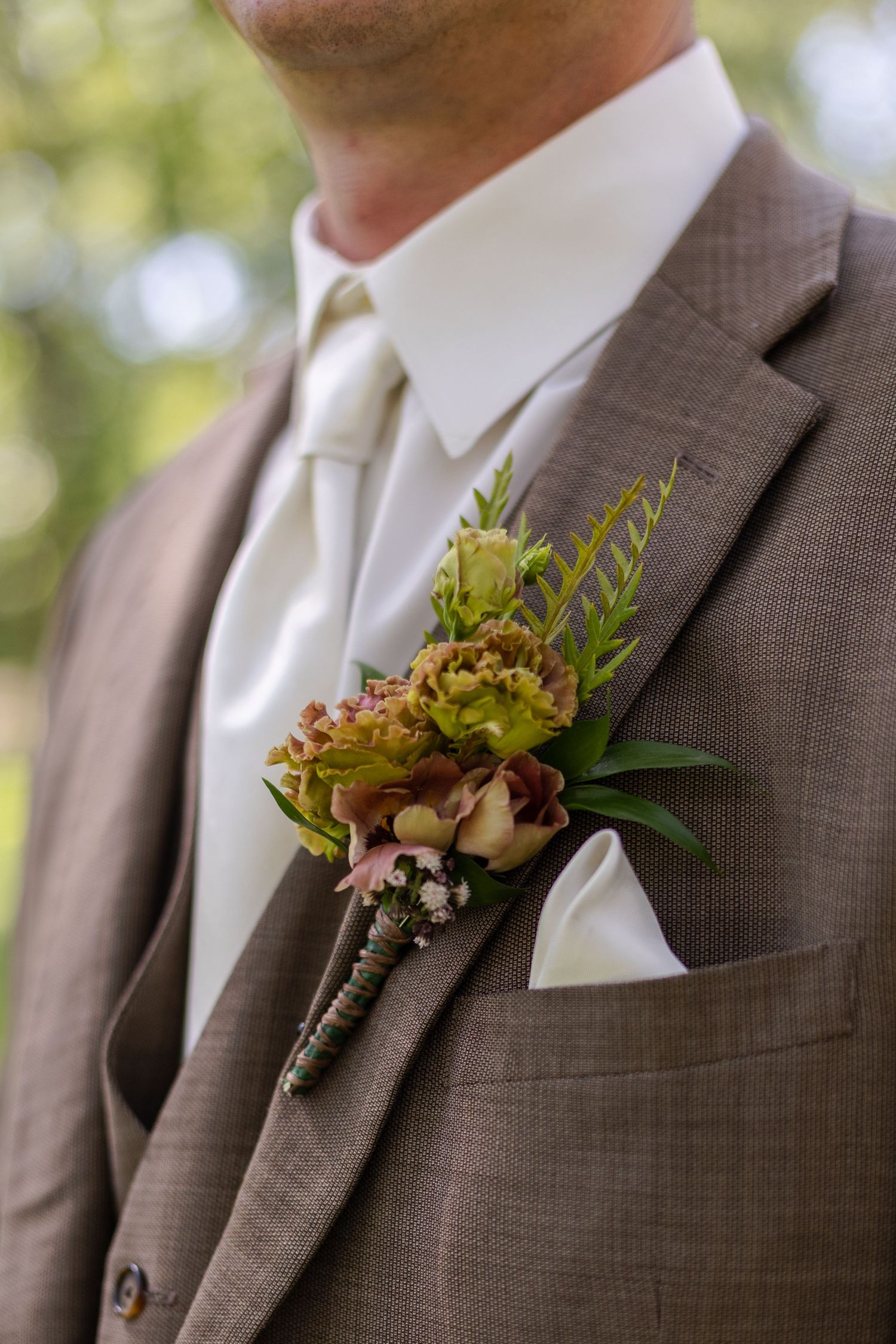 Close-up details of autumn-toned boutonnieres on brown suit lapels.