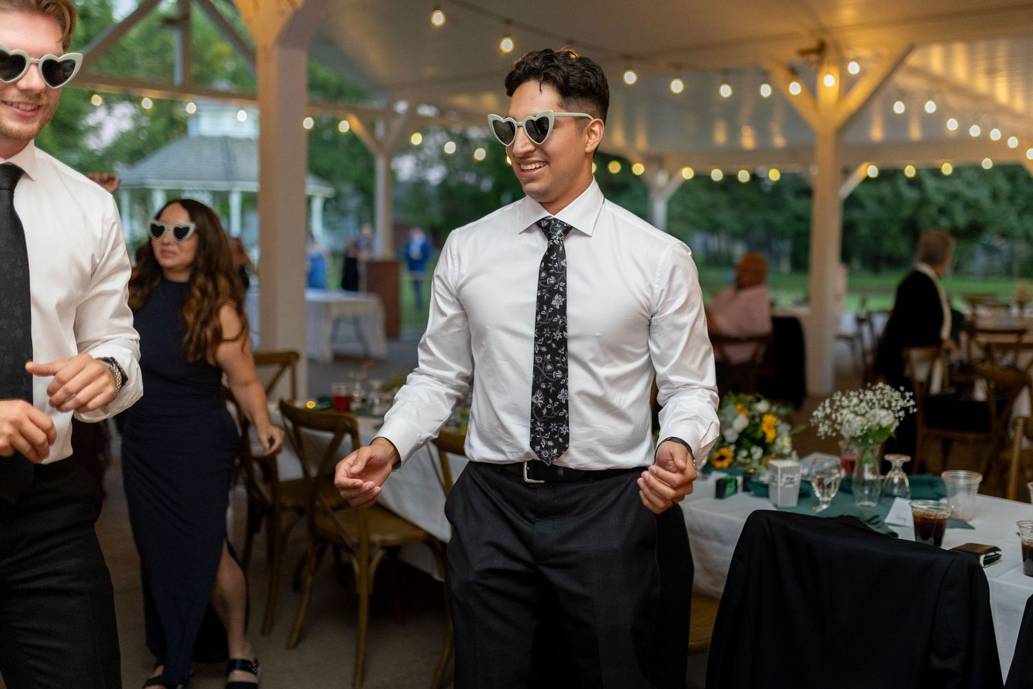 Wedding reception guests dancing and celebrating in an outdoor venue with string lights.