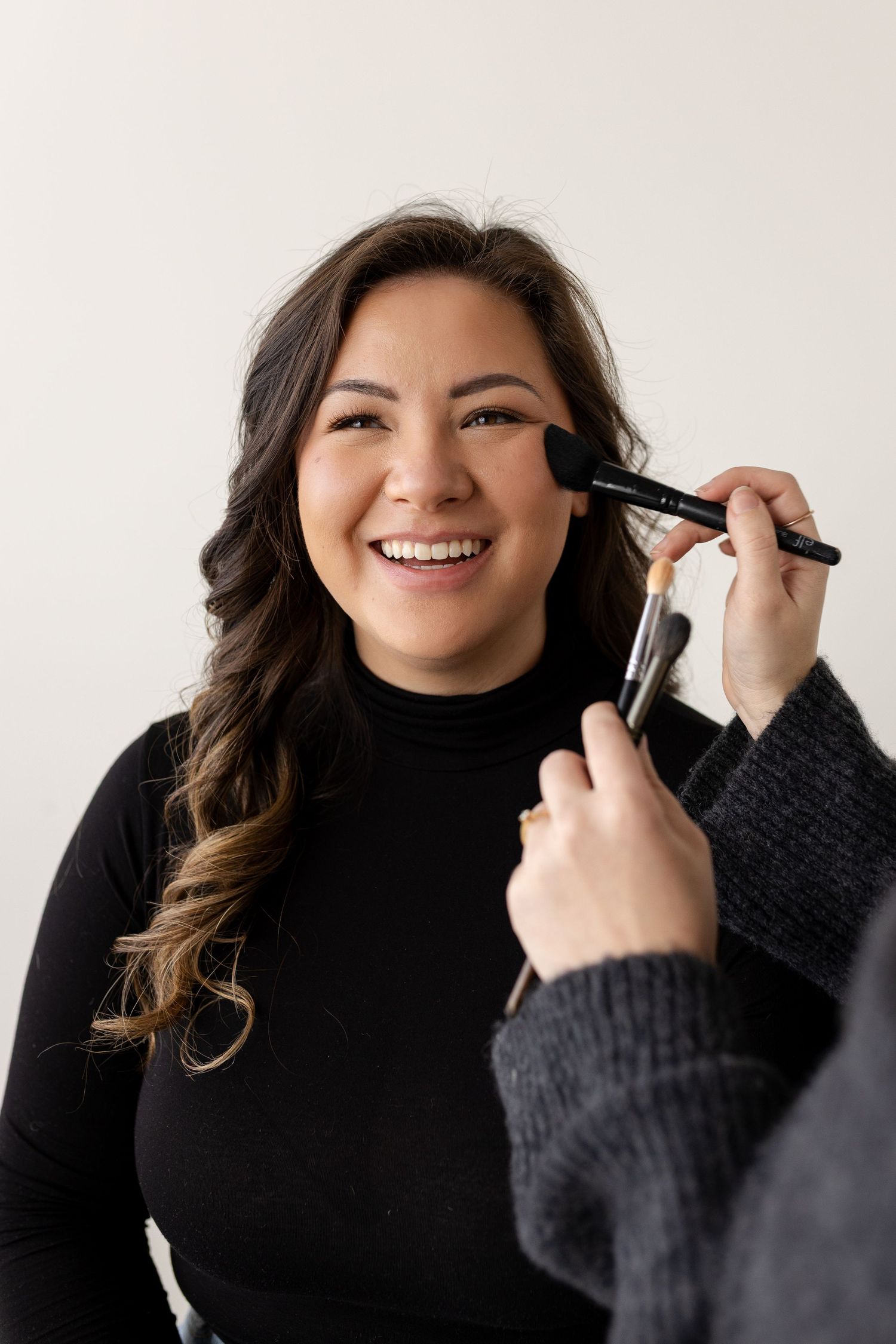Person in black turtleneck smiling and applying makeup in a series of four connected photos.