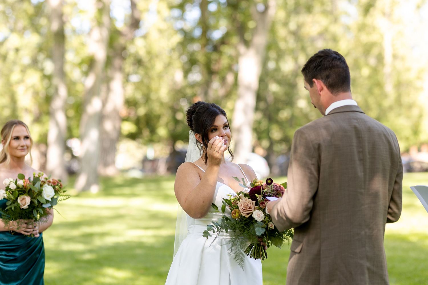 Elegant outdoor wedding ceremony in a sunlit park with guests seated on white chairs.