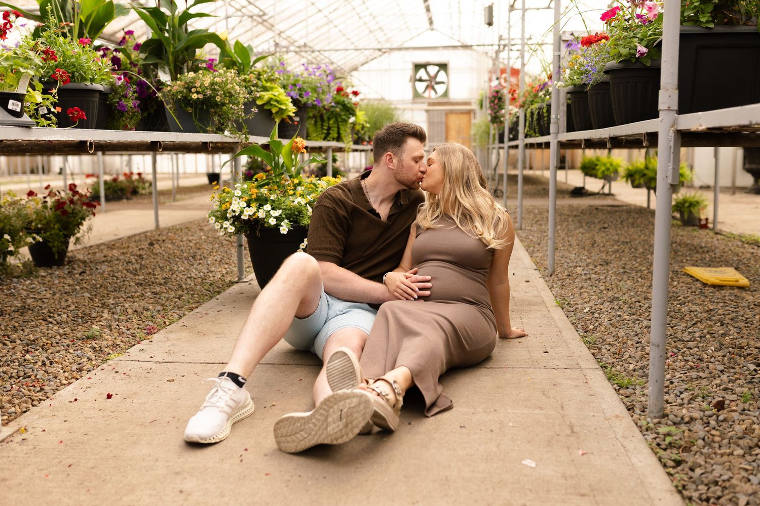 Side view of couple resting on greenhouse floor with plants in background.