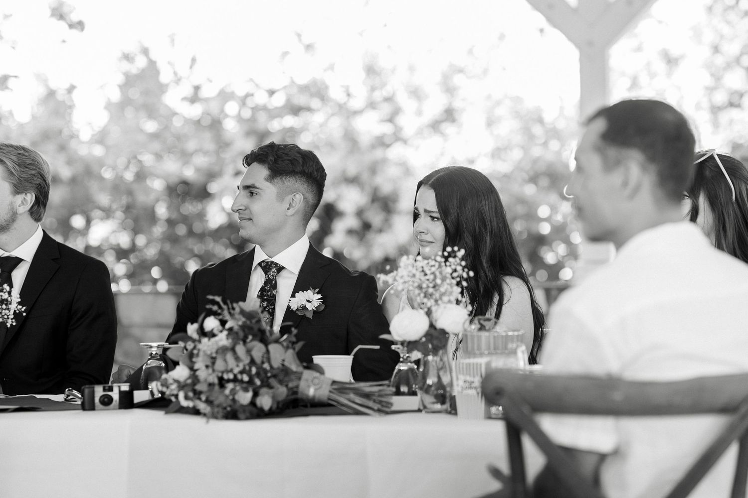 Wedding reception guests seated at tables with white linens enjoy dinner and conversation outdoors at dusk.