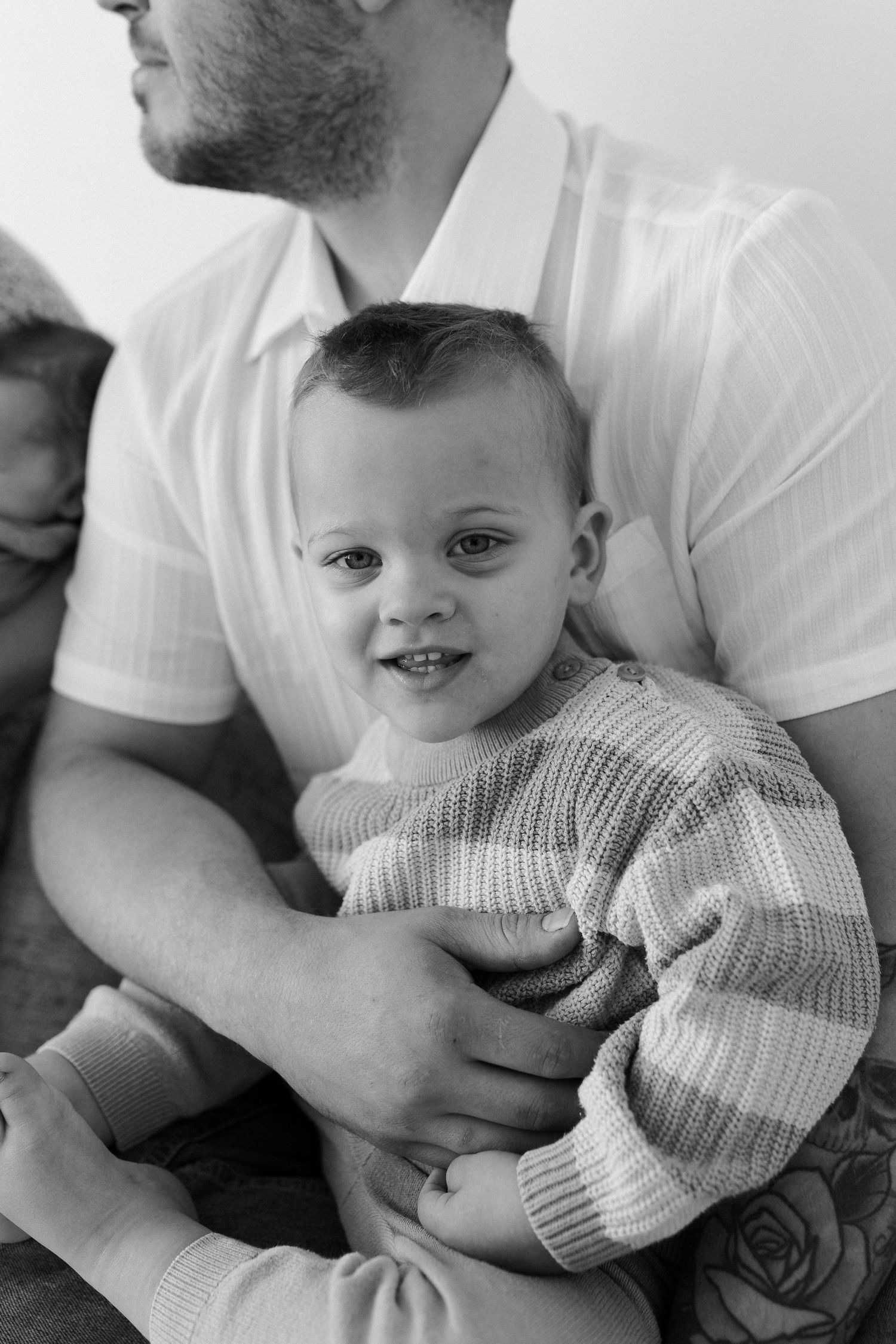 A series of black and white photos showing a baby in a knit sweater being held and cuddled.