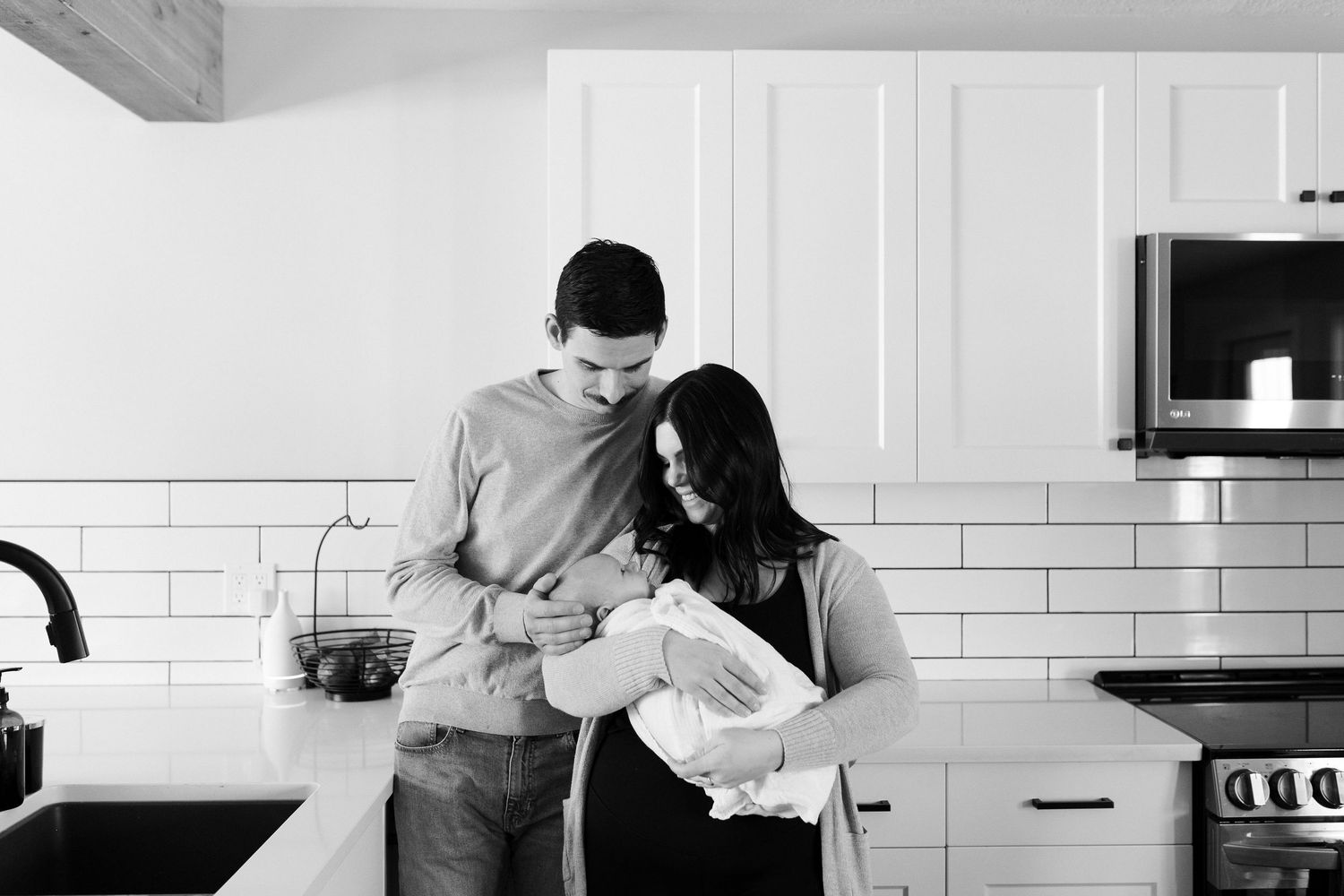 Black and white photos of a family sharing tender moments in their white modern kitchen.