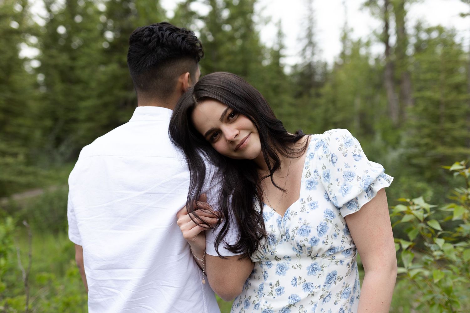A romantic outdoor portrait of a couple embracing among evergreen trees.