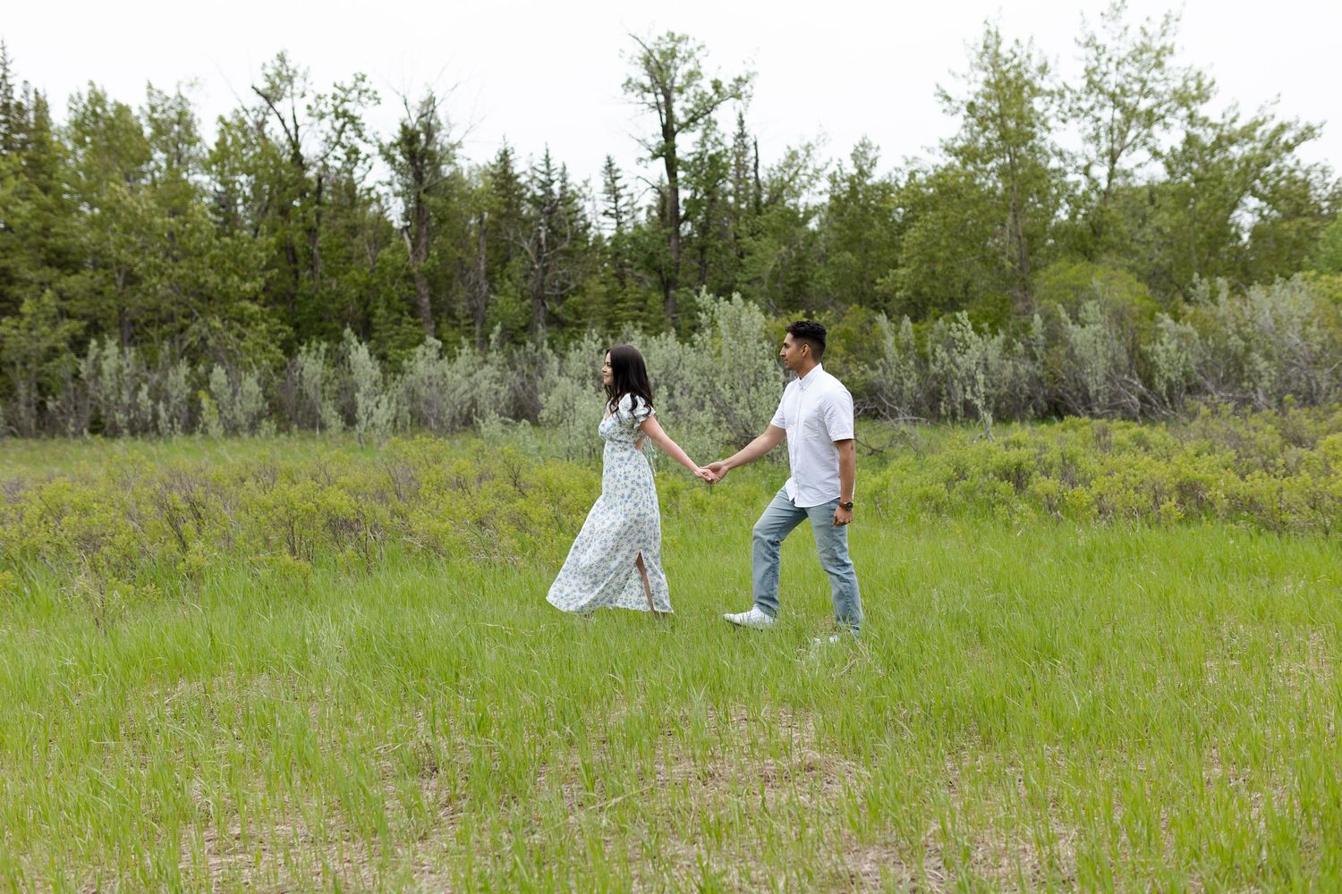 Two people walking together across a grassy meadow with trees in the background.