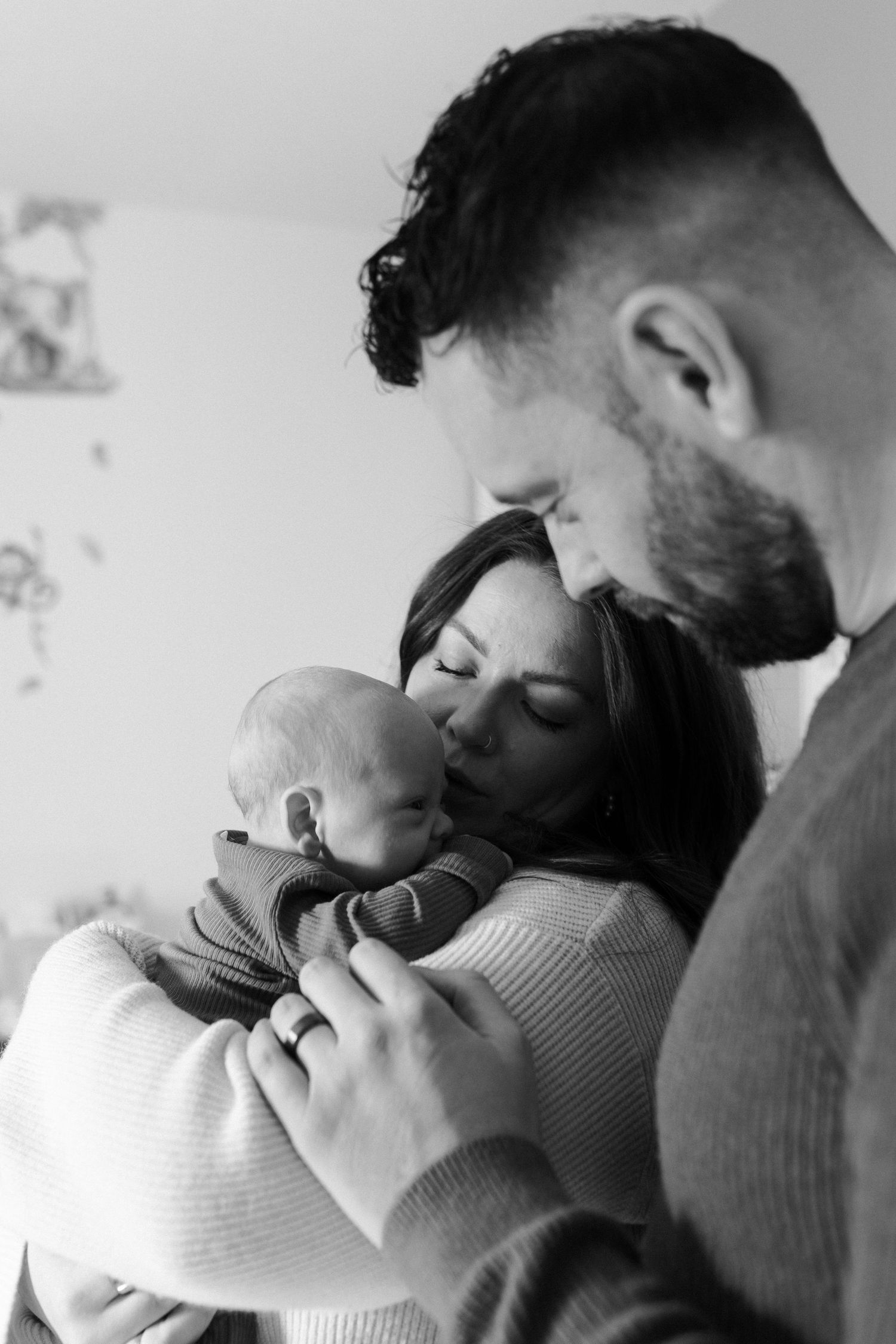 A tender black and white portrait of parents embracing their newborn baby in a soft, intimate moment.