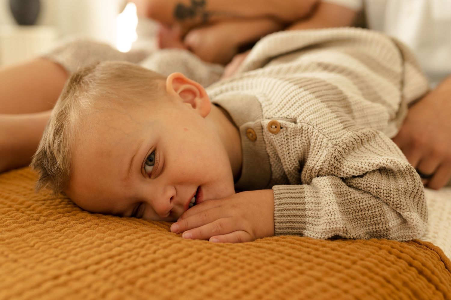 A small child rests peacefully on a mustard yellow blanket while wearing a cozy beige sweater.