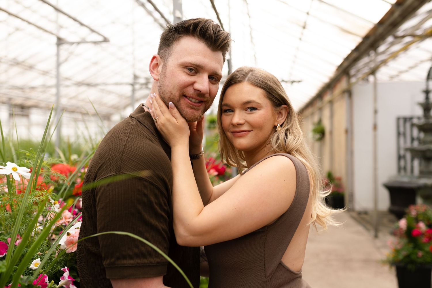 Romantic greenhouse maternity session with couple sharing tender moments among flowers.