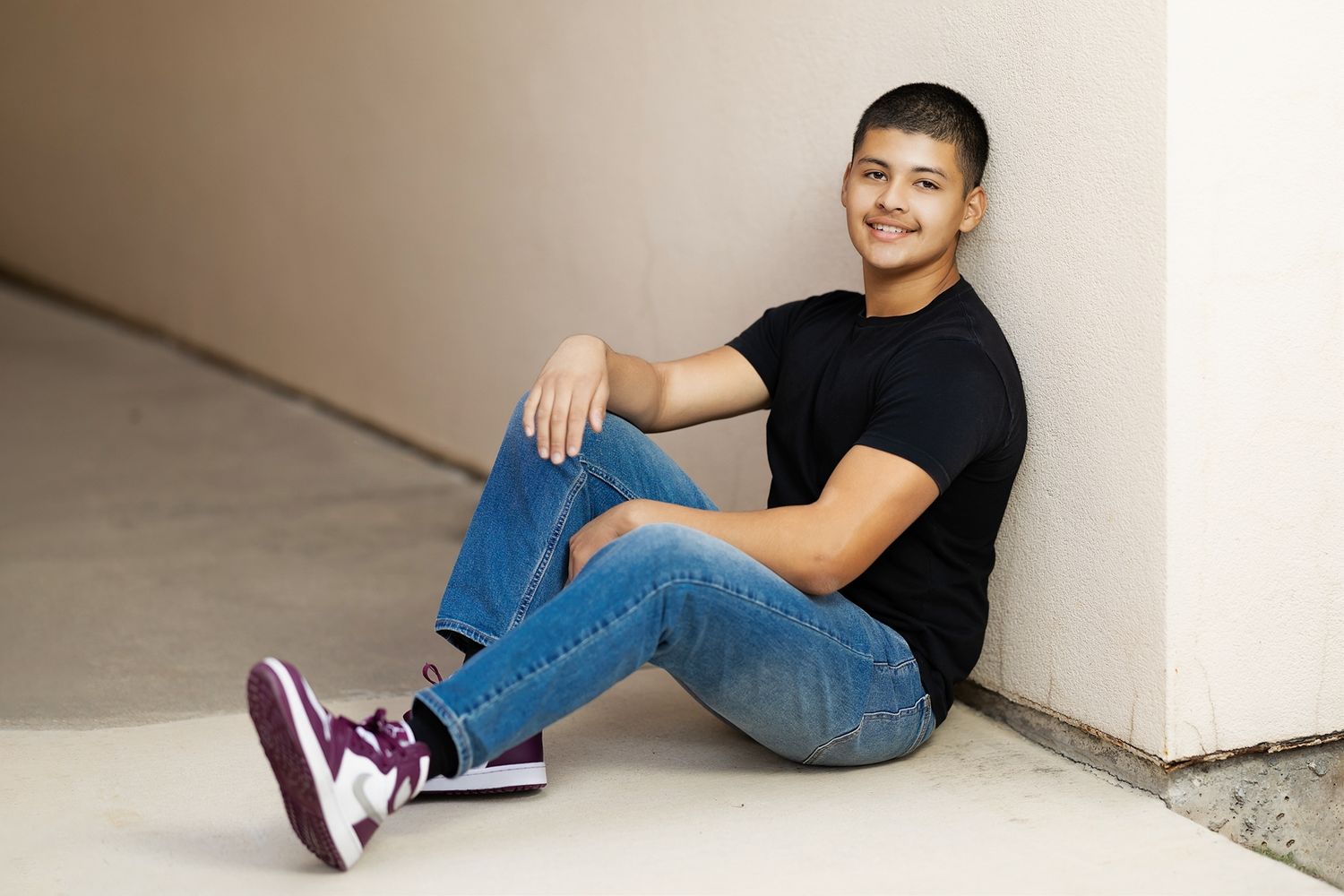 Person in black t-shirt and jeans sitting against white wall showing different casual poses.