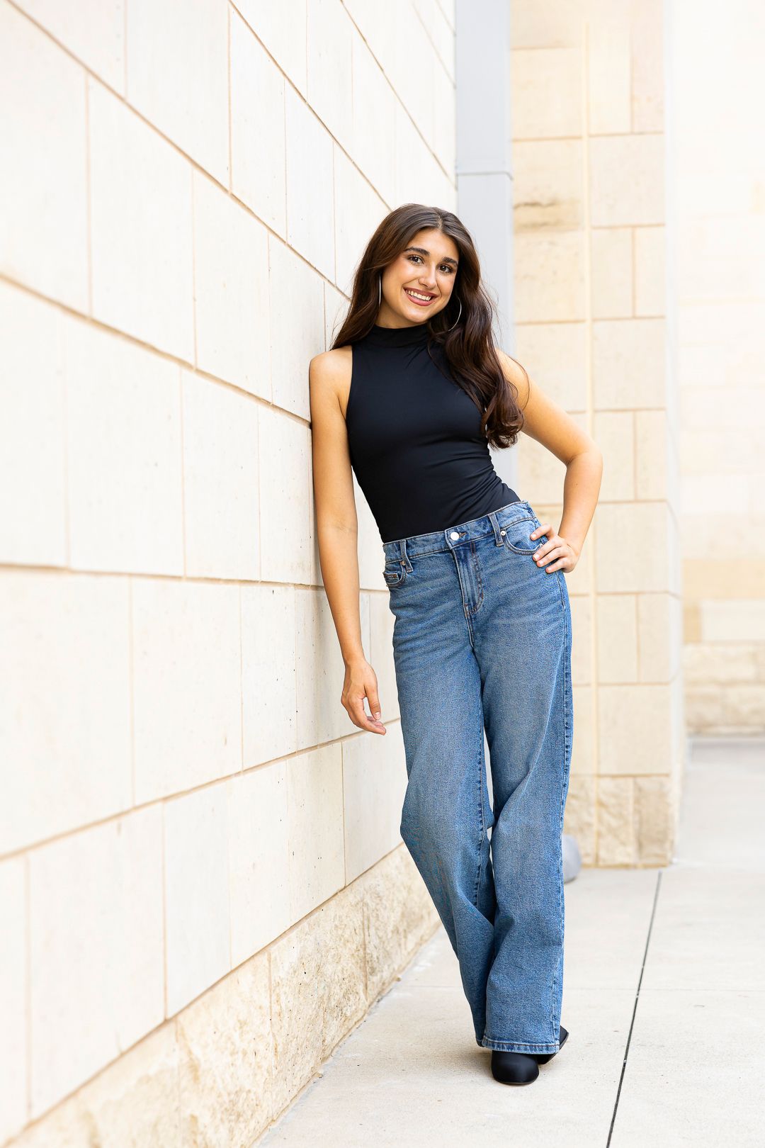 Modern fashion poses against a geometric white wall wearing denim and black top.