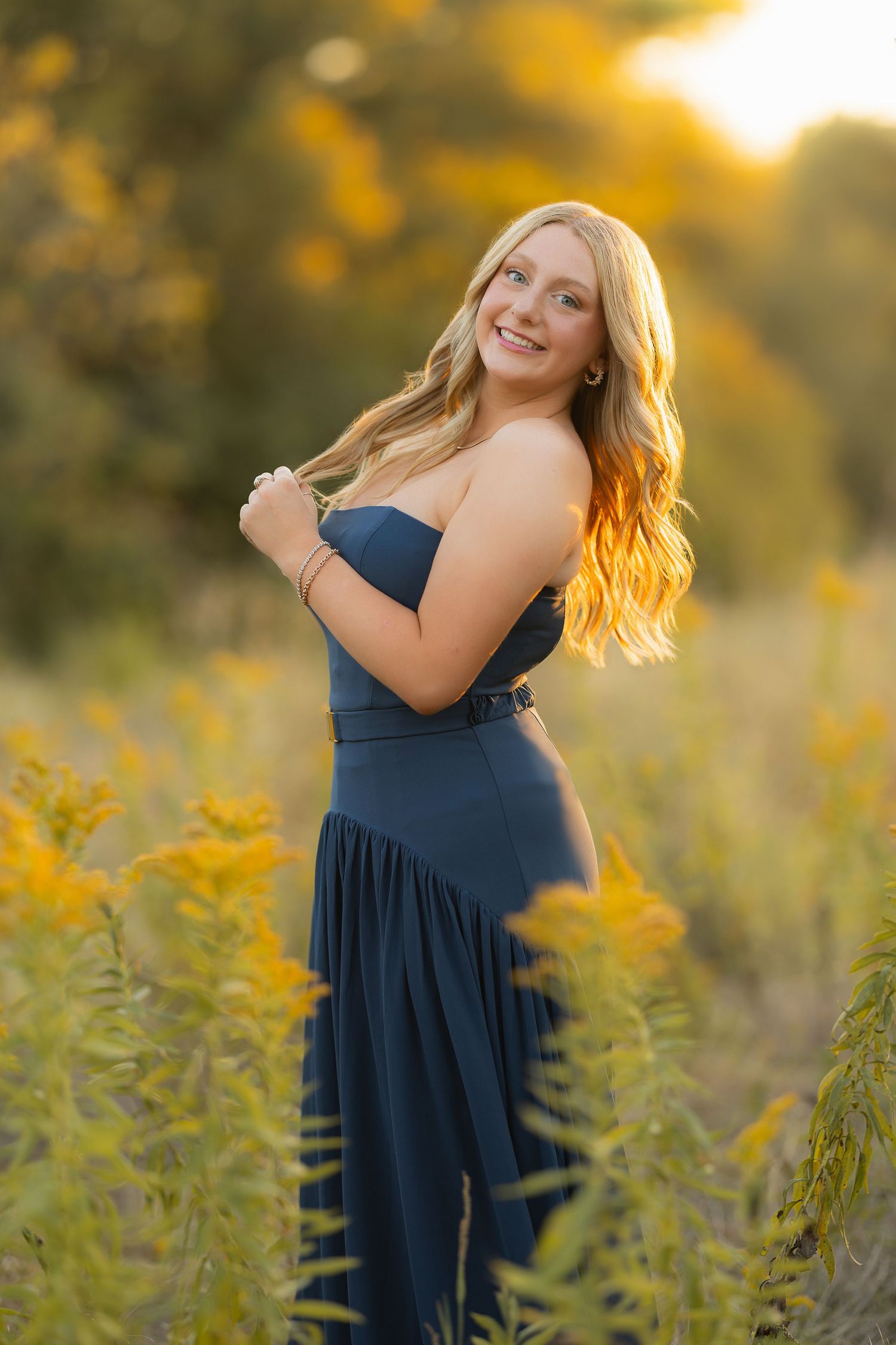 A navy blue dress stands out beautifully against golden wildflowers during a glowing sunset photoshoot.