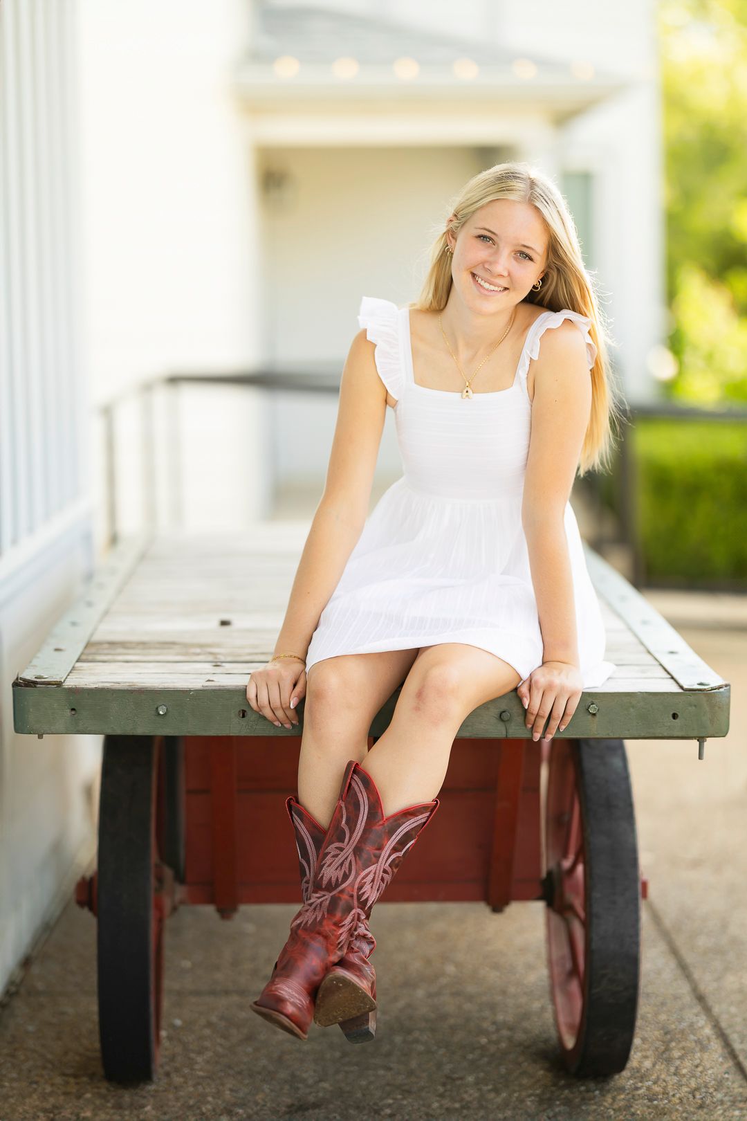 A person in a white dress sits on a wooden deck wearing brown cowboy boots.