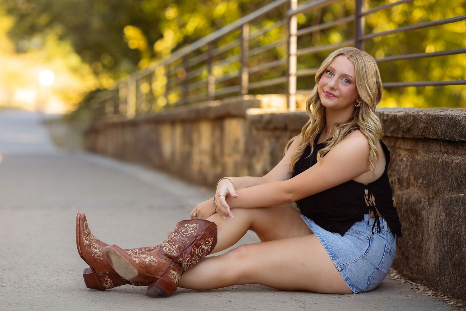 A person in cowboy boots and denim shorts sits on stone steps during golden hour lighting.