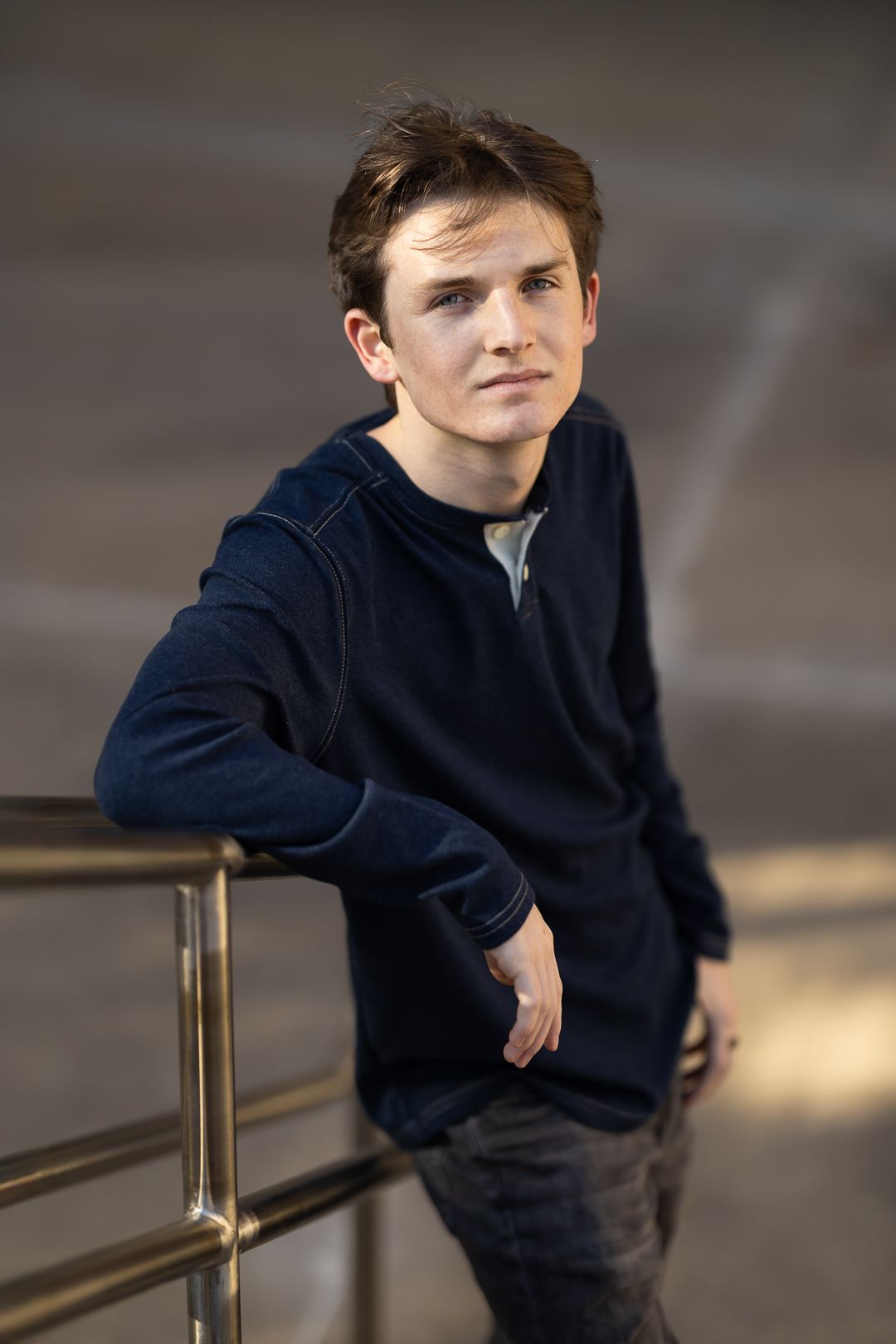 A person in a navy sweater leans casually against a metal railing in an indoor setting.