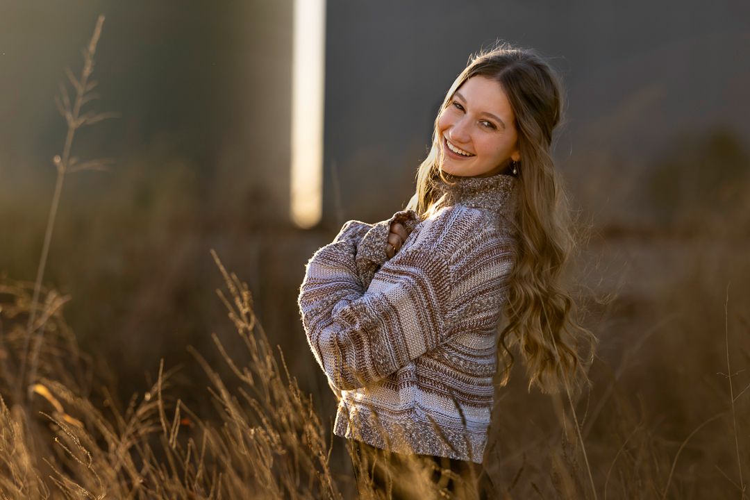 Person in gray knit sweater poses against golden field at sunset creating warm autumn vibes.
