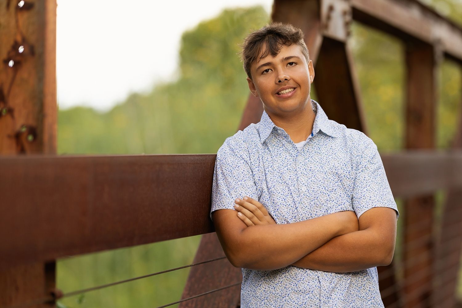 Person wearing a blue patterned shirt stands against a wooden structure in an outdoor setting.