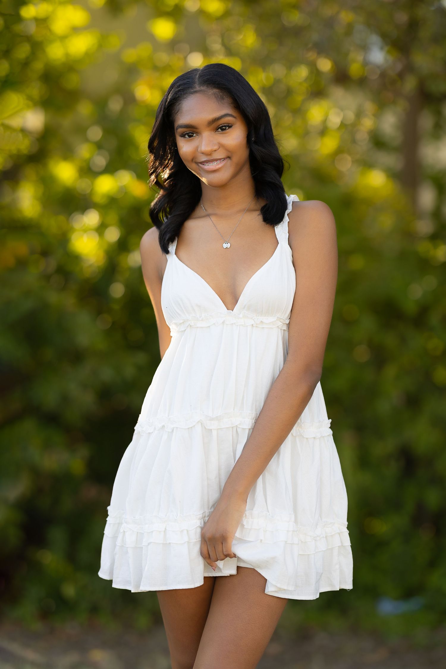 A summer portrait featuring a white tiered sundress against a soft bokeh background of yellow and green foliage.