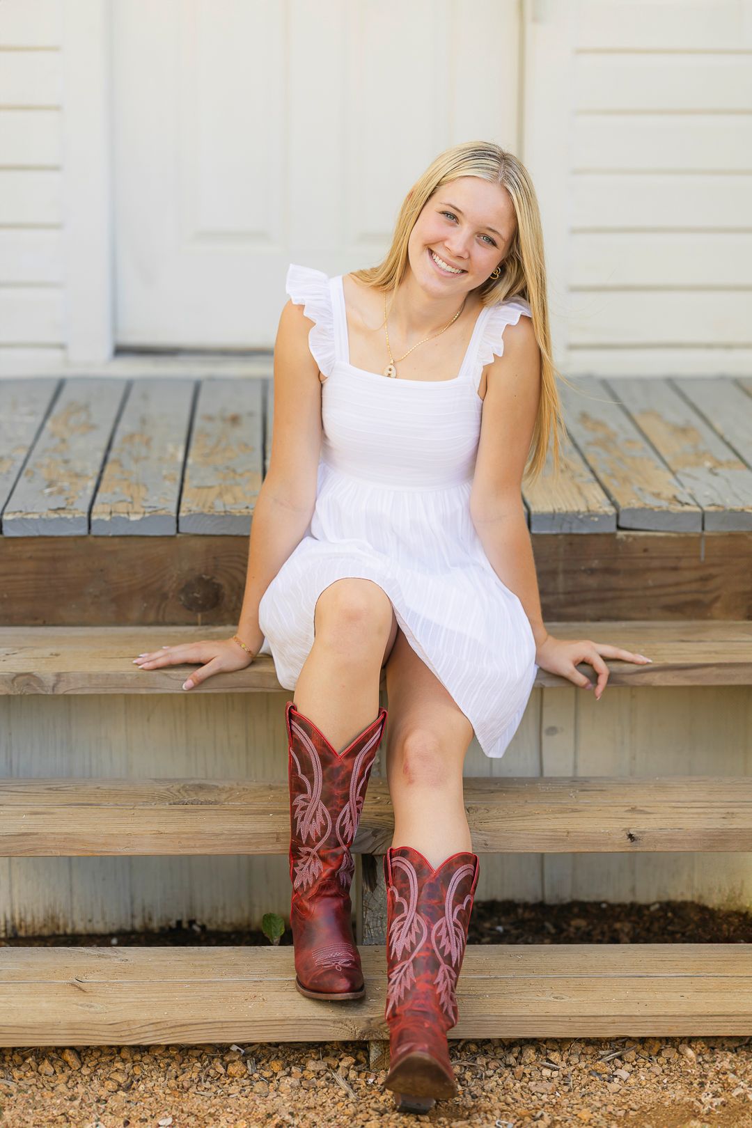 Someone wearing a white dress and red cowboy boots sits on wooden steps.
