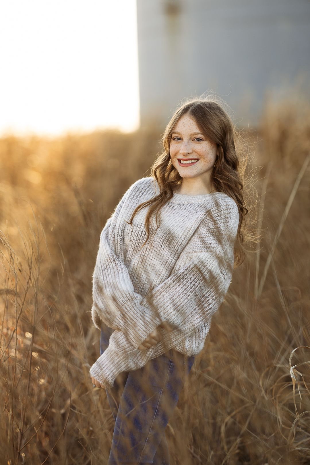 A person wearing a cozy beige sweater poses in a golden wheat field at sunset.