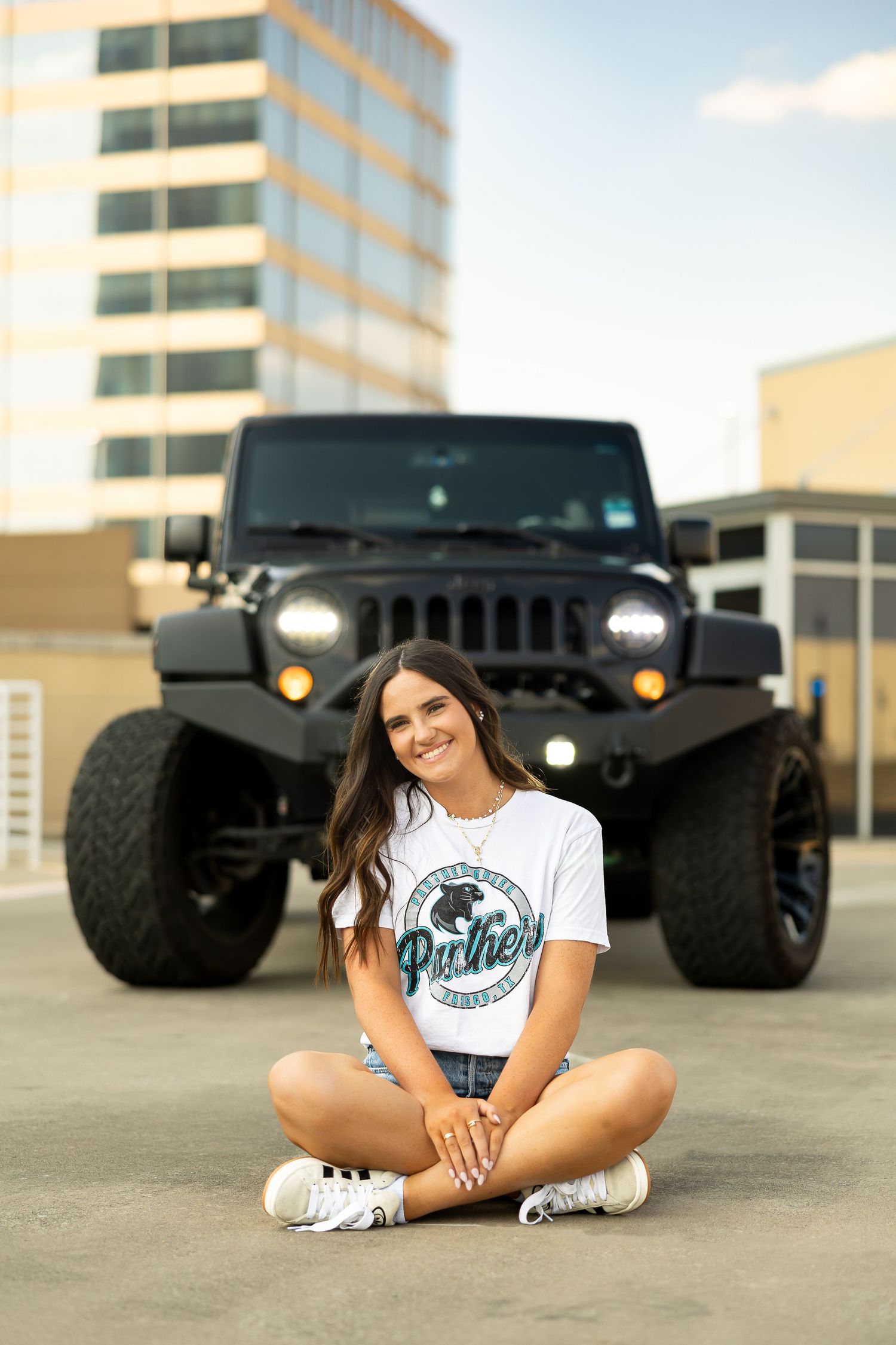 A lifted black Jeep Wrangler parked in front of a building with someone sitting cross-legged on the ground.